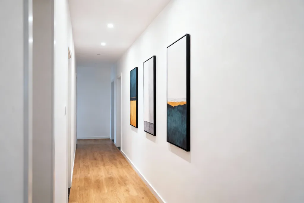 Modern wall art prints displayed in a minimalist white hallway with black frames and light wood flooring