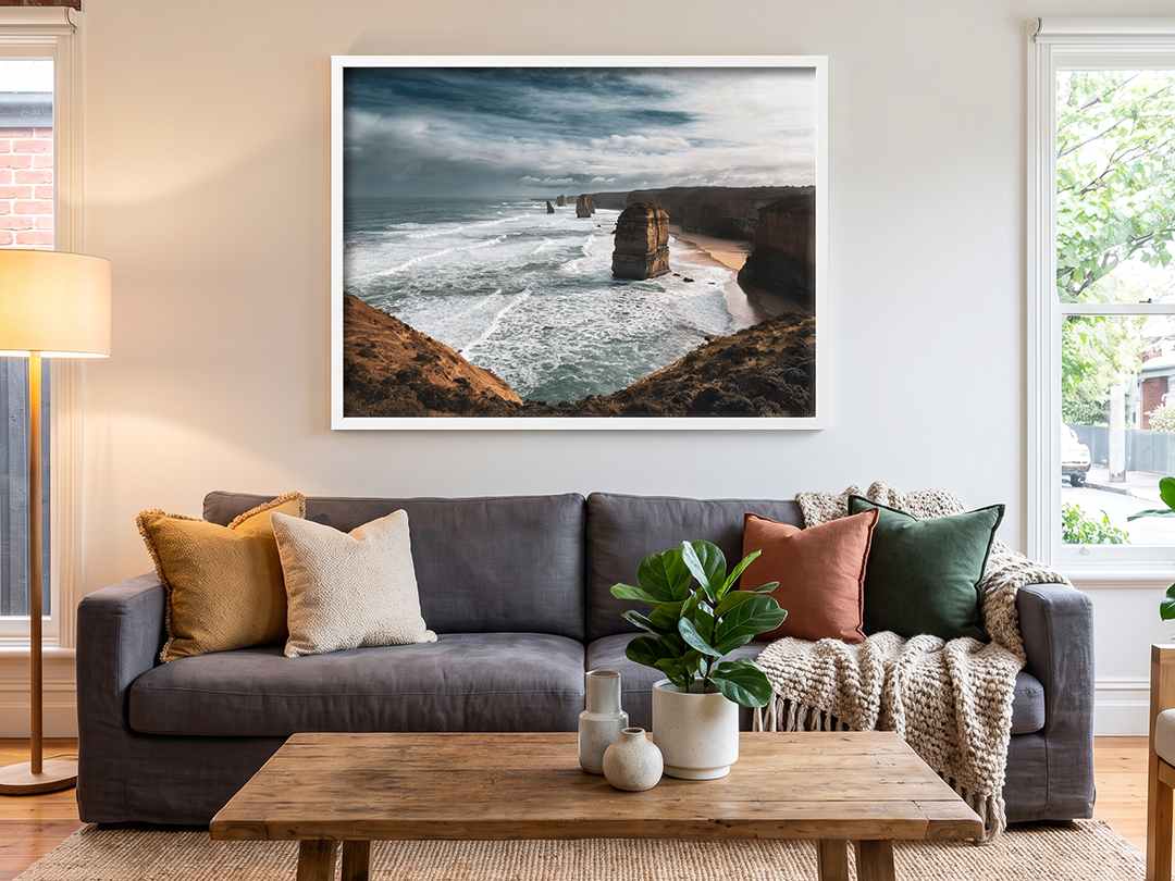 Large ocean-cliff photograph displayed above a charcoal sofa