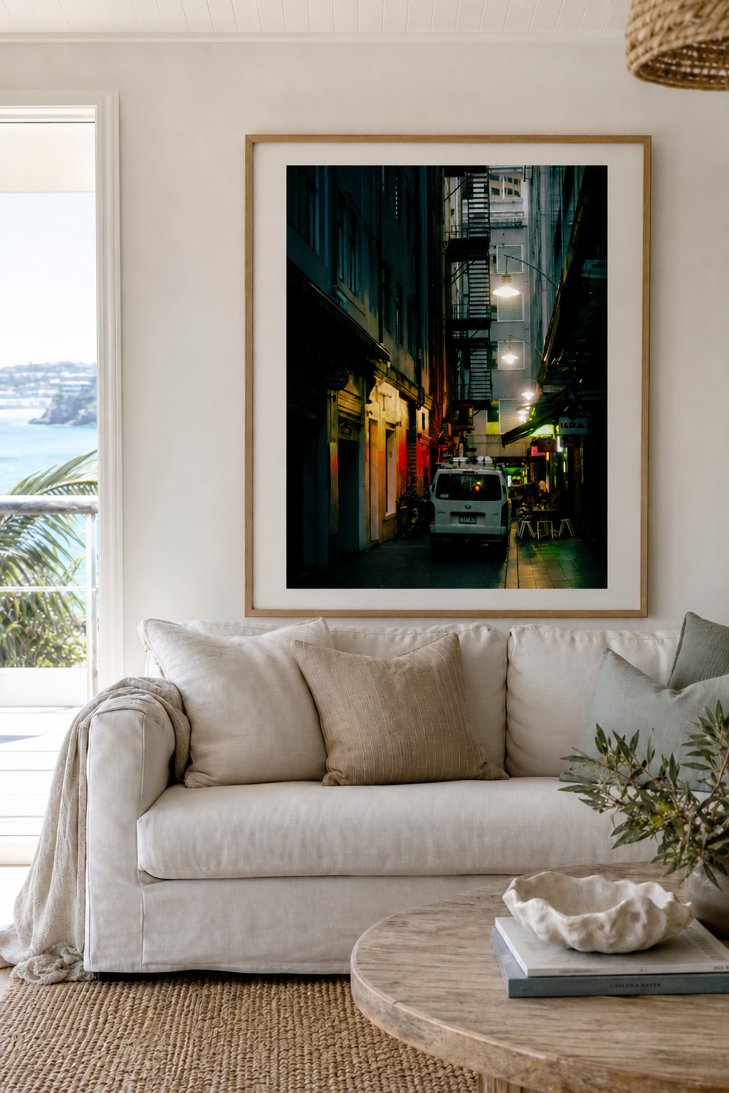 Vertical city laneway wall art in a timber frame above a white sofa